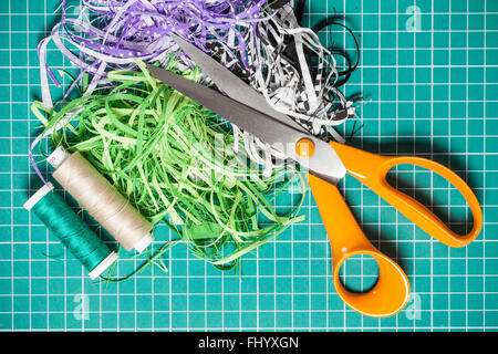 Textile offcuts, threads and scissors on checkered rotary cut mat Stock Photo