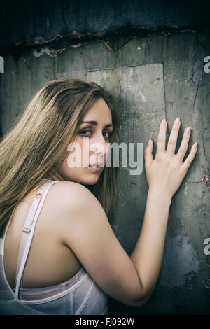 Scared young woman leaning against the wall Stock Photo