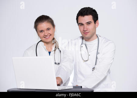 two young doctors, male and female in white coats, with stethoscope working with laptop pc Stock Photo