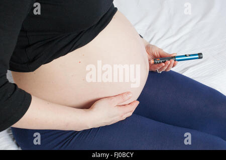 A nine month pregnant woman injects short acting insulin (Novorapid)  into her stomach to control her Type 1 diabetes. Stock Photo