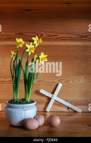 Pot of daffodils with palm cross and three eggs on pine wood. Stock Photo