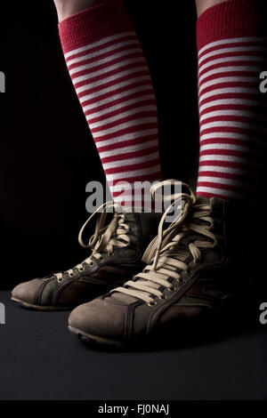 Woman’s legs with sneakers and a pair of red socks with white stripes on dark background Stock Photo