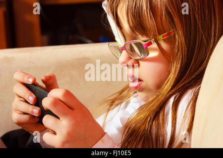 Technology generation. Little girl child in glasses with medicine plaster playing games on smartphone mobile phone at home Stock Photo
