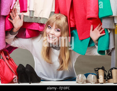 Pretty woman sitting on the floor under clothing from wardrobe. Young happy undecided shopper girl bought new clothes.Shopaholic Stock Photo