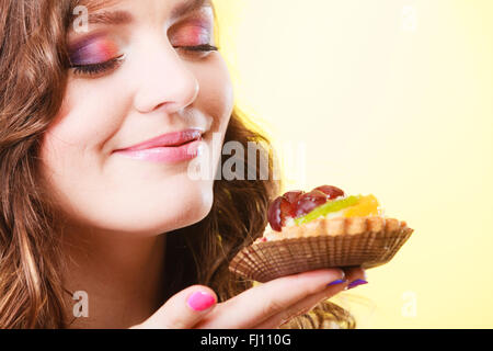 Bakery sweet food indulging and people concept. Cute attractive woman closed eyes holds cake cupcake in hand smelling on yellow. Stock Photo