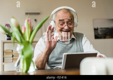 Senior man using mini tablet and headphones for skyping at home Stock Photo