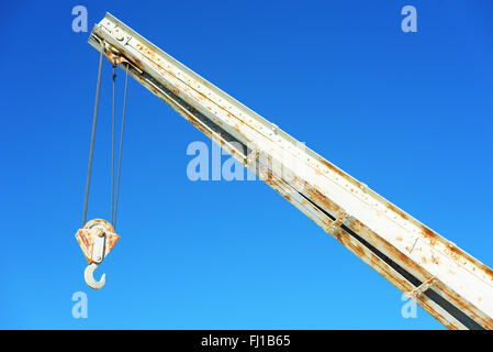 The arm and hook of an old steel crane against a clear blue sky. Rust has begun to grow on the metal. Stock Photo