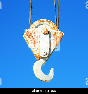 Detail of an old hook on a steel crane against a clear blue sky. Rust has begun to grow on the metal. Stock Photo