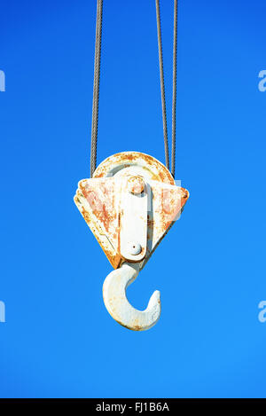 Detail of an old hook on a steel crane against a clear blue sky. Rust has begun to grow on the metal. Stock Photo