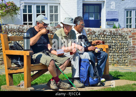 Three male  walkers rest on a seat for a cup of tea in the village of  Itchenor, Chichester Harbour, West Sussex, England, UK