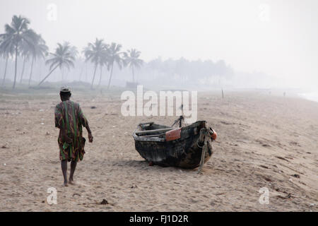 A man walks on the beach of Ouidah , Benin , alone , in the early morning near a typical boat / canoe Stock Photo