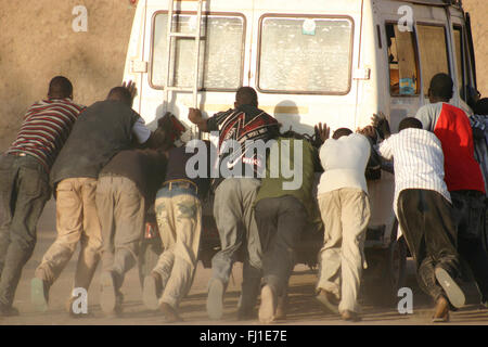 A group of black man are pushing together a broken down vehicle in Djenné , Mali Stock Photo