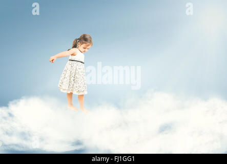 Cute little girl standing barefoot and watching down on clouds Stock Photo