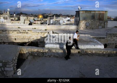 Two Jewish men walk by sunset on the roofs of Jerusalem old city , Al-Aqsa Mosque in the distance Stock Photo