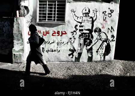 Banksy painting , woman walks in Dheisheh refugee camp - Bethlehem - Palestine Stock Photo