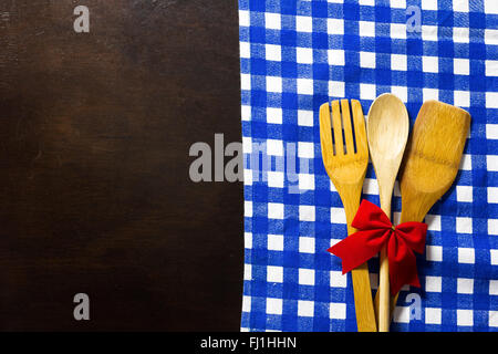 Wooden table with checked tablecloth and wooden kitchen utensils with red ribbon Stock Photo