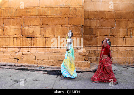 two women are carrying water in metal jugs in the street of Jaisalmer, India Stock Photo