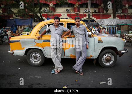 Two taxi cab drivers in  grey uniform are waiting for customers in front of classical yellow taxi at Howrah railway station , Kolkata , India Stock Photo