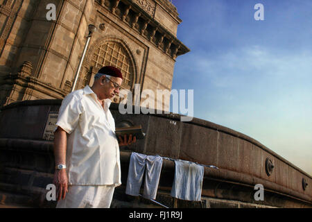 A man reads a book in the early morning light at the Gateway of India, Colaba , Mumbai, India Stock Photo