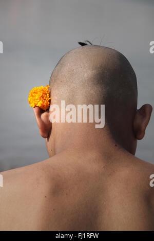 A bald shaved man pilgrim meditates in haridwar, India, with flower on his head Stock Photo