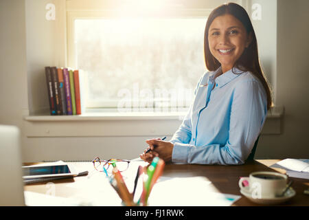 Successful business woman sitting at her desk in a office smiling at the camera Stock Photo