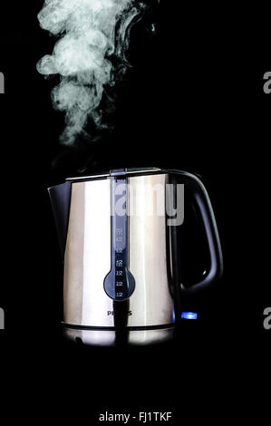 Stainless steel kettle on a black background, with steam. Stock Photo