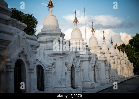 MANDALAY, Myanmar — Rows of pristine white kyauksa gu (stone-inscription caves) stretch across the grounds of Kuthodaw Pagoda. Built in 1857 by King Mindon, the complex contains 729 marble slabs that collectively form what is known as the World's Largest Book. Each small stupa houses a marble tablet inscribed on both sides with text from the Tipitaka, the complete Pali Canon of Theravada Buddhism. The orderly arrangement of these structures reflects traditional Buddhist architectural principles. Stock Photo