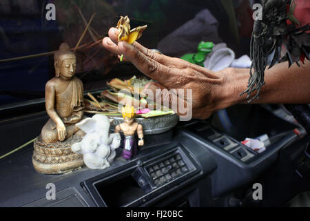 Man / Hand blessing a car in Bali before taking the road with statues of Buddha, Ganesh and Dragon Ball , Indonesia Stock Photo