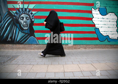A woman walks along a striking mural on the wall of the former US embassy / US Den of Espionage in Tehran, Iran Stock Photo