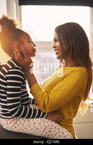 Black woman caressing her daughter in a warm home, backlit sun Stock Photo