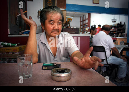 Portrait of a old man in Kuala Lumpur sitting in a restaurant and smoking a cigarette Stock Photo