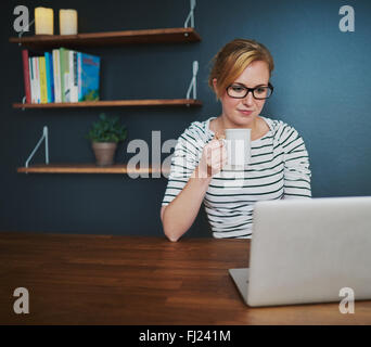 Female entrepreneur working at desk using laptop drinking coffee and looking serious Stock Photo