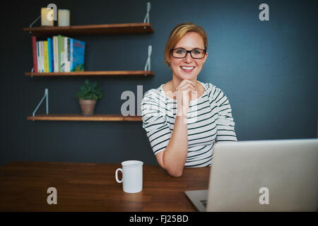 Confident female entrepreneur at office smiling at camera sitting with a laptop Stock Photo