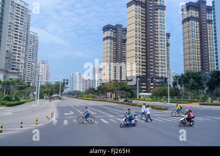 Pedestrians and bikers crossing a road in Xiuying, Haikou, Hainan, China. Skyline in the background. Stock Photo