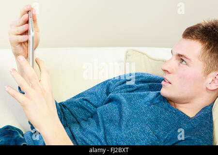 Modern technology home and relaxation concept. Young man with pc computer digital tablet on couch Stock Photo