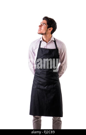 Young chef or waiter posing, wearing black apron and shirt isolated on white background, looking up to a side Stock Photo