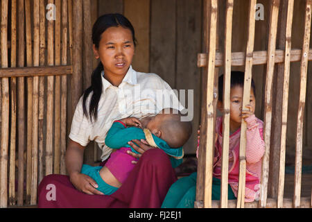 A woman of the AKHA tribe nurses a child in her bamboo house -  village near KENGTUNG or KYAINGTONG - MYANMAR Stock Photo