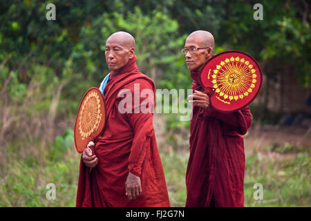 BUDDHIST MONKS with fans walk along the road - BAGO, MYANMAR Stock Photo