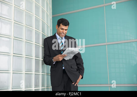 Happy Indian businessman looking down and reading a newspaper. Stock Photo