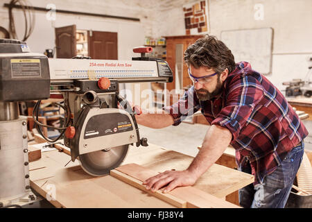 Carpenter using radial arm saw to cut wood in workshop Stock Photo
