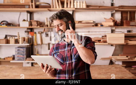 Man with beard in woodwork studio using phone and tablet Stock Photo