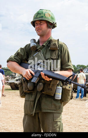 Vietnam War period re-enactment. American soldier on guard duty standing in sunshine holding M16 rifle, and two canteens hanging from belt. Stock Photo