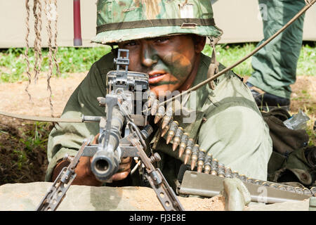 Vietnam war re-enactment. Close up. American soldier with camouflage paint on face, aiming M60 machine gun directly at viewer. Eye-contact. Stock Photo