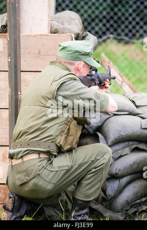 War and peace show, England. Vietnam war re-enactment. American fire base under attack by unseen enemy in woods, soldiers behind wire returning fire. Stock Photo