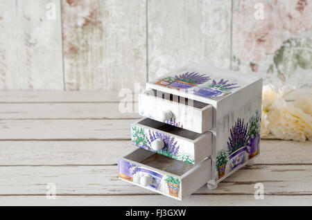 A handmade chest of trinket drawers decoupaged with vintage paperwith pots of Lavender on a rustic wooden background Stock Photo