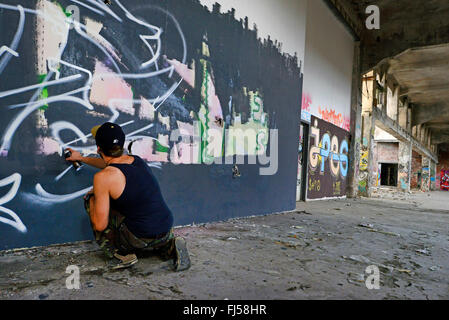 man spraying graffiti at a wall in an abandonend industrial ground, Germany, North Rhine-Westphalia, Duesseldorf Stock Photo