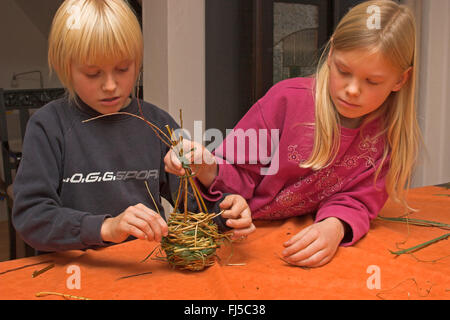nesting material for ball nest, two children braiding willow branches, Germany Stock Photo