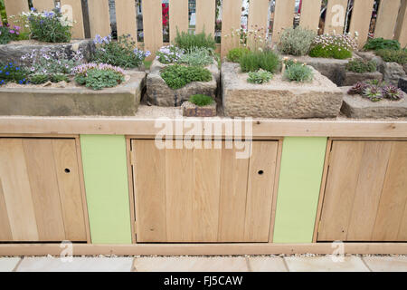 Patio with a rock garden with alpine plants plant in stone containers container trough troughs bench with storage cupboards - spring UK Stock Photo