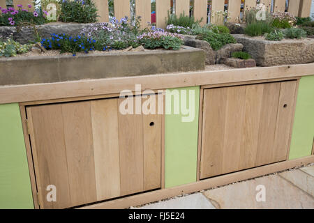 Patio with a rock garden with alpine plants plant in stone containers container trough troughs bench with storage cupboards - spring UK Stock Photo