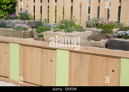 Patio with a rock garden with alpine plants plant in stone containers container trough troughs bench with storage cupboards - spring UK Stock Photo